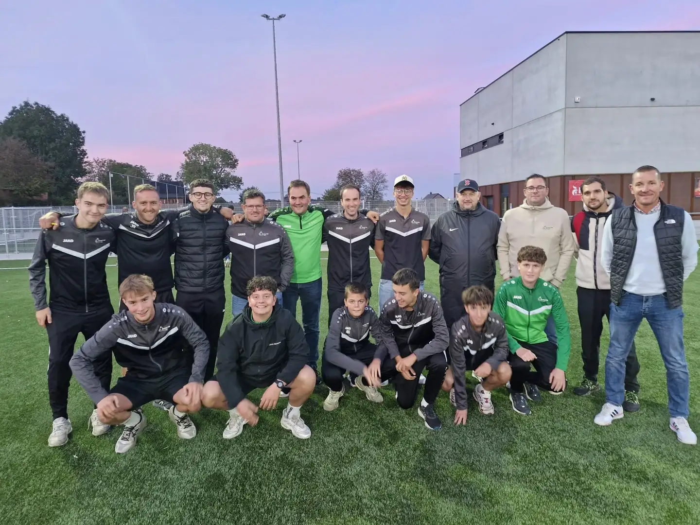Groupe de formateurs et d'encadrants du club réunis sur le terrain au coucher du soleil.